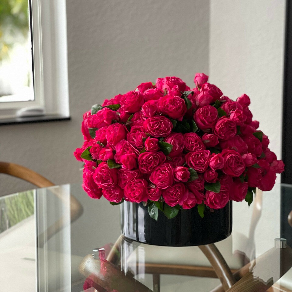 Rosas inglesas de color rosa oscuro en macetero de vidrio negro.